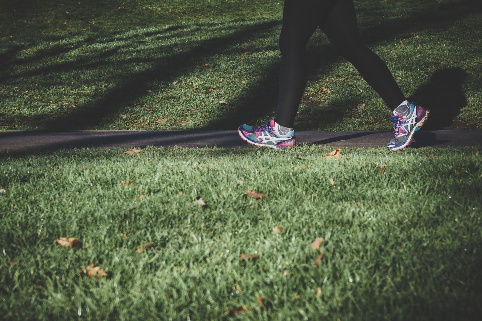 person in black leggings and sneakers running in grass